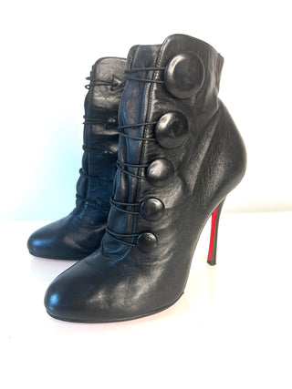 A pair of Christian Louboutin Booton black leather ankle boots with lace-up front detailing, large decorative buttons, and a high stiletto heel with a signature red sole.