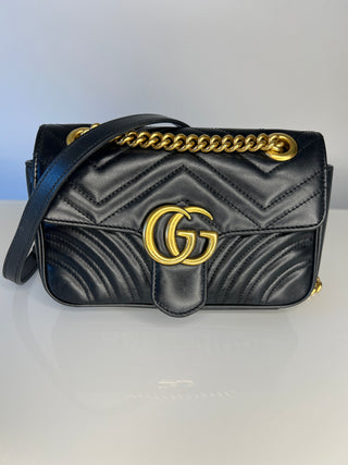 Gucci GG Marmont small black quilted leather shoulder bag with gold-tone hardware, featuring the iconic interlocking G logo on the front flap and a gold chain