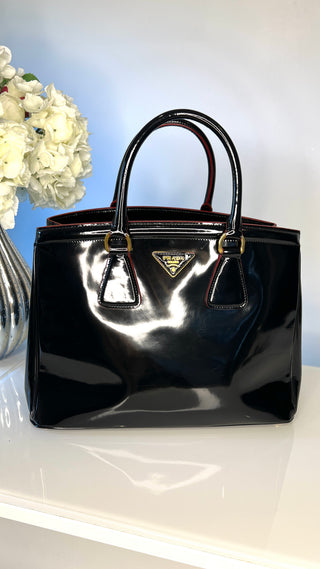 Black glossy handbag with Prada logo on a white surface with a light blue background