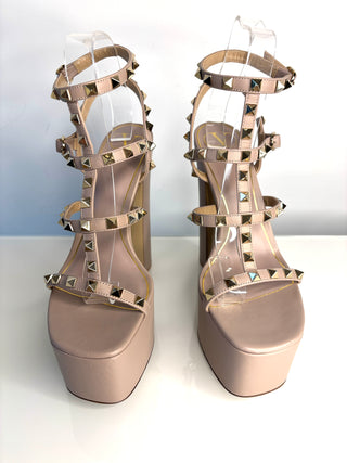 Pair of beige high-heeled sandals with studded details on a white background