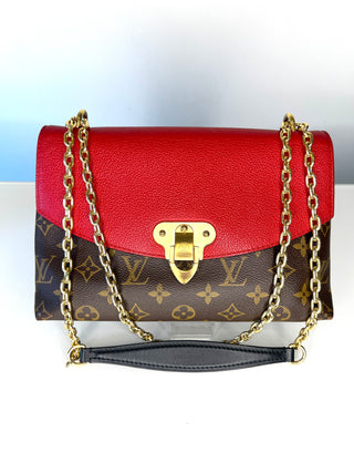 A Louis Vuitton shoulder bag featuring a vibrant red pebbled leather top flap and a brown monogram canvas body, accented with gold-tone hardware and a black leather wristlet strap.