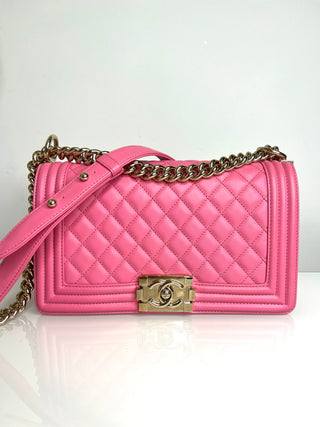 Pink quilted handbag with gold chain and clasp on a white background