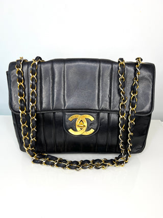 A black quilted leather vintage Chanel Jumbo flap shoulder bag with a gold-tone interlocking CC logo and a black-and-gold chain strap.