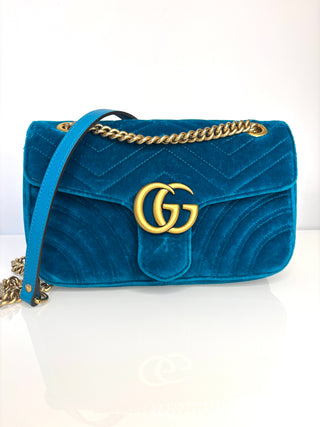 Blue velvet handbag with gold chain and logo on a white background