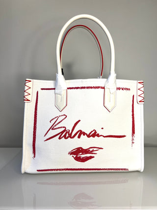 White handbag with red accents and Balmain logo on a gray background