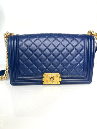 A Chanel Boy Bag navy blue quilted leather shoulder bag with a gold-tone chain strap and a prominent gold-tone interlocking CC clasp.