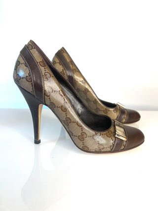 A pair of Gucci high-heeled pumps featuring the brand's signature GG monogram canvas in brown and beige, accented with dark brown leather trim and a small silver buckle on the toe.