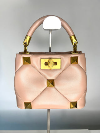 Blush Pink top handle handbag with gold stud accents on a stand against a gray background