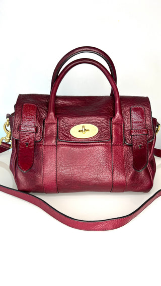 Maroon leather handbag with gold postman's lock clasp on a white background