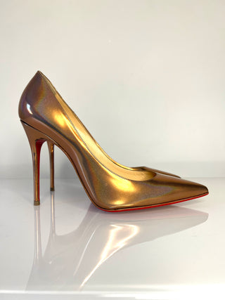 Gold high-heeled shoe on a reflective surface with a white background