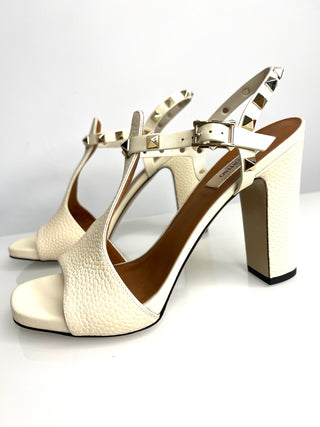 White high-heeled sandals with gold straps on a white background