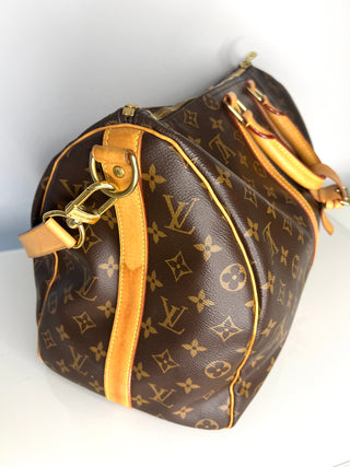 Designer handbag with monogram pattern and gold accents on a white background