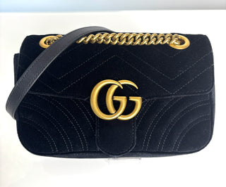 Black quilted handbag with gold chain strap and logo on a white background