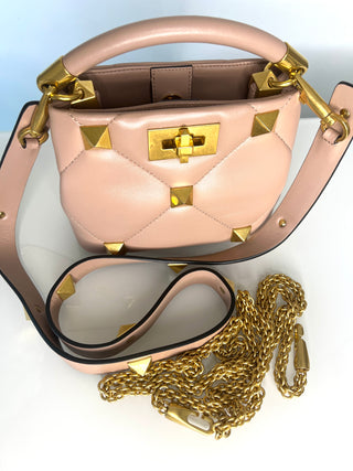 Pink handbag with gold accents and chain detail on a light blue background