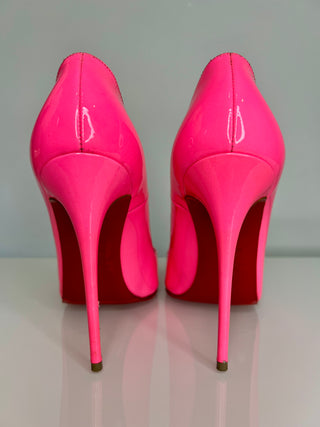 Pair of bright pink high-heeled shoes on a reflective surface with a neutral background