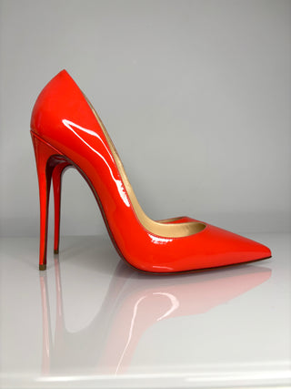 Shiny red high-heeled shoe on a reflective surface with a gray background