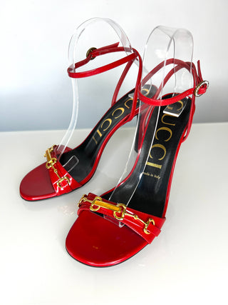 Red high-heeled sandals with gold horsebit accents on a white background