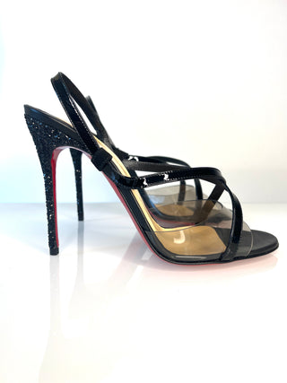 A pair of Christian Louboutin black patent leather slingback sandals with transparent PVC uppers, a glittery black stiletto heel.