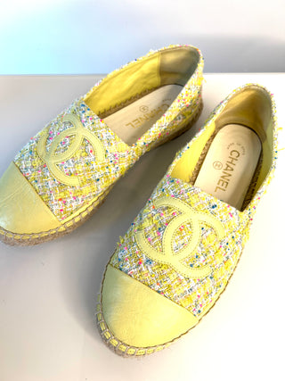 A pair of Chanel espadrille slip-on shoes in pale yellow tweed with multicolored flecks, yellow leather toe caps, and braided jute soles. The Chanel logo is embossed on the toe and the brand name is visible on the insole.