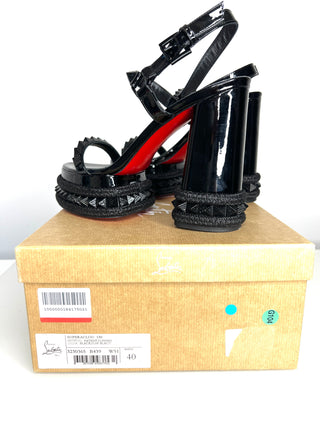 Black high-heeled sandals with red soles on a beige shoe box