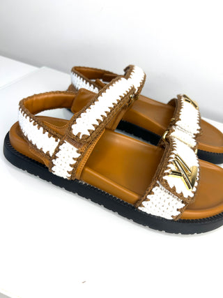 Brown sandals with white textured straps on a light gray background
