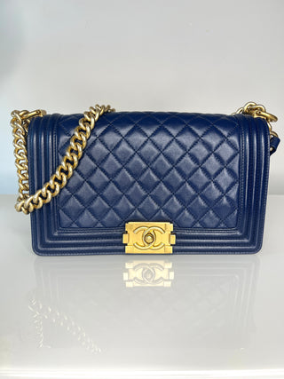 A Chanel Boy bag navy blue quilted leather shoulder bag with gold-tone hardware, featuring a diamond-quilted pattern, a flap closure, and a gold chain strap.