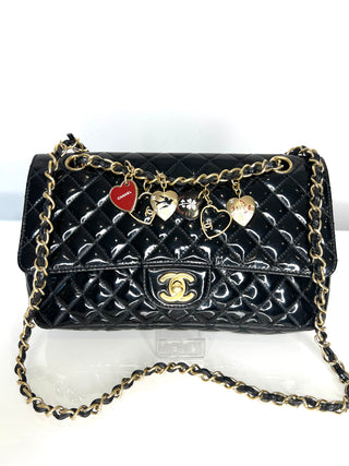 Black quilted handbag with gold chain and charms on a white background