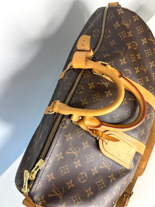 Designer handbag with monogram pattern and gold accents on a light gray background