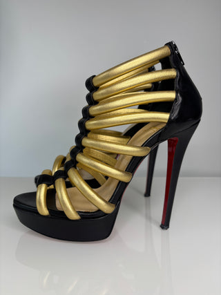 Black high-heeled sandal with gold straps on a white background