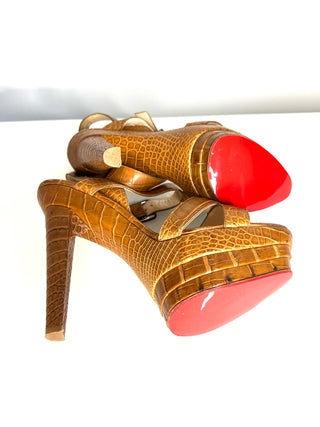 High-heeled shoes with red soles and gold lizard skin pattern on a white background