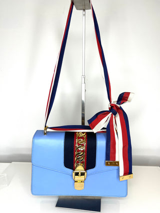 Light blue handbag with a colorful strap on a white background