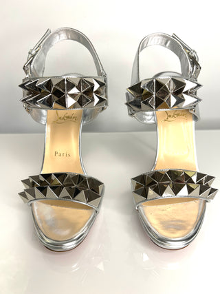 Pair of silver high-heeled sandals with pyramid studs on a white background