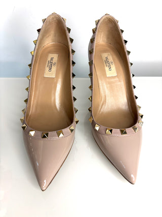 Pair of beige high-heeled shoes with studded details on a white background