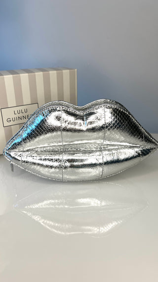 Silver lip-shaped clutch on a white surface with a gray background
